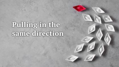 Pulling in the same direction - Curved arrangement of white paper boats led by a red boat