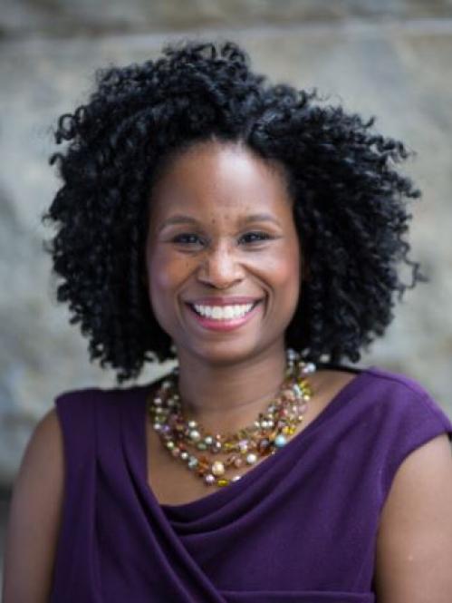 Nyeema is an african american woman with freckles and curly hair. She us smiling and wearing a purple blouse and a gold multicolored necklace.